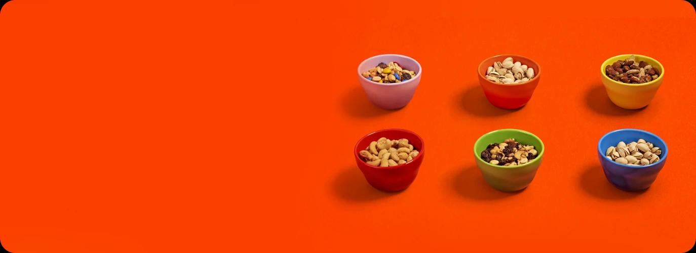 Cashews, pistaccios, and mixed nuts are displayed in colorful bowls against an orange surface